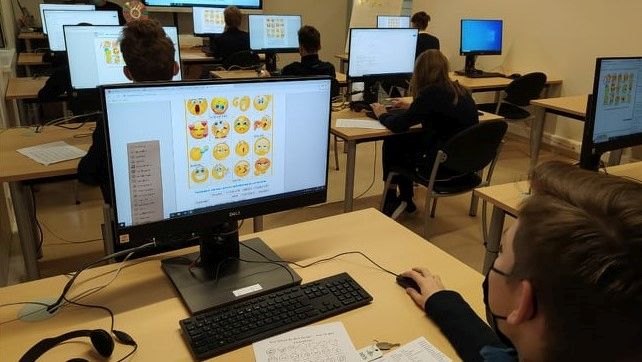 Keletas veikiančių kompiuterių monitorių ir jais dirbantys mokiniai