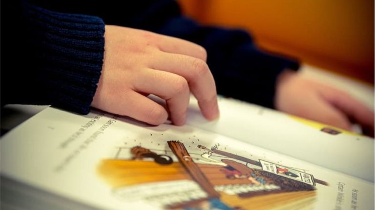 Vaikas laiko ranką ant atverstos knygos