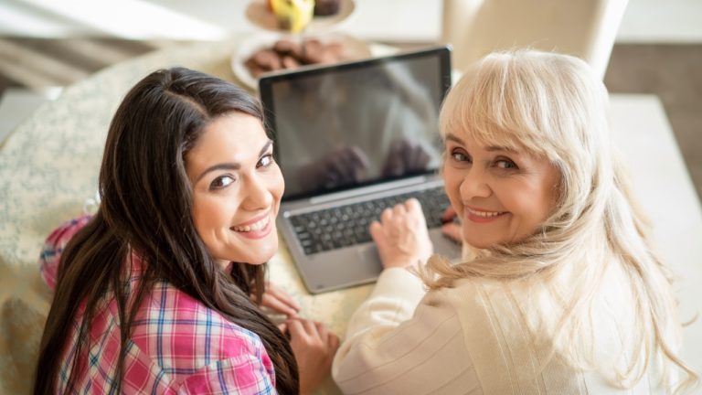 Jauna ir vyresnė moterys šypsosi atsisukusios nuo kompiuterio