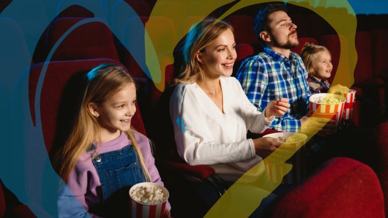 Mergaitė, moteris, vyras ir berniukas žiūri į kino ekraną ir šypsosi