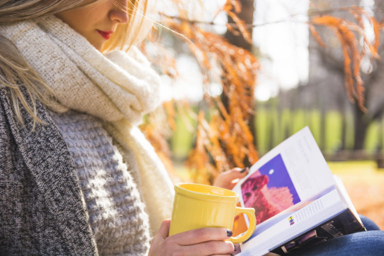Mergina laiko puodelį ir knygą rudens spalvų ir saulės fone