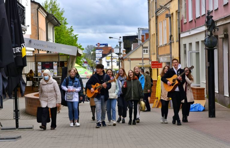 Būrys jaunuolių eina gatve, groja gitaromis, dainuoja