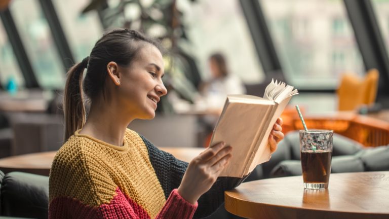 Mergina šypsosi ir skaito knygą bibliotekos fone