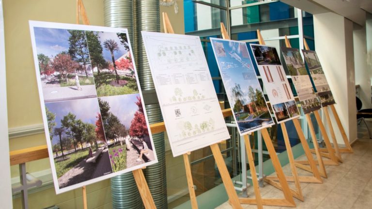 Ant medinių stovų stovi stendai su architektūrinėmis idėjomis