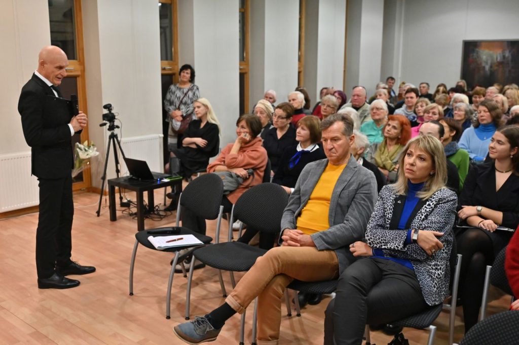 Stovi aktorius Albinas Kėleris, sėdi gausi auditorija renginio dalyvių