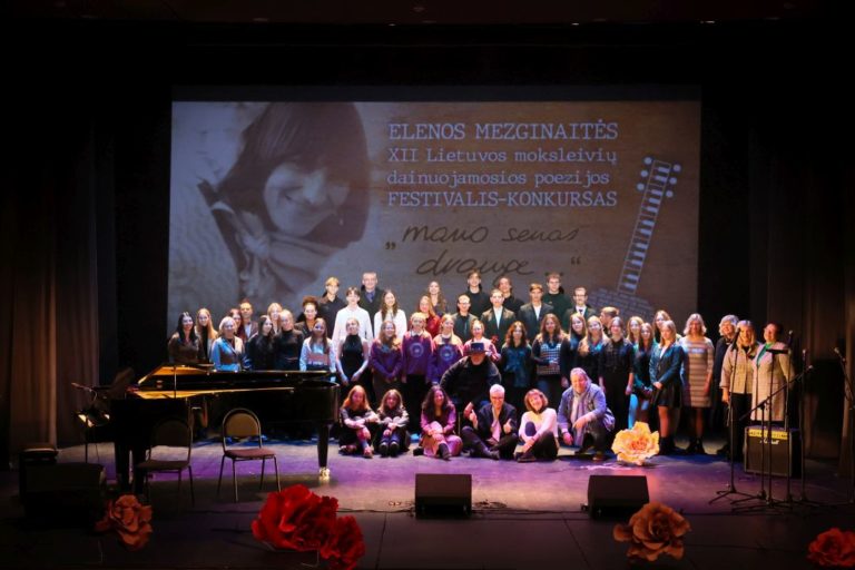 visi festivalio dalyviai, muzikantai, rengėjai, komisijos nariai ant teatro scenos E. Mezginaitės portretinės nuotraukos fone