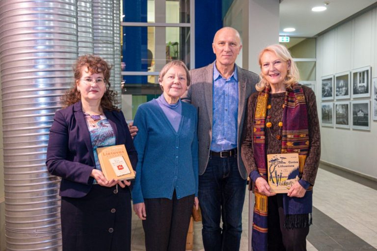 Trys moterys ir vienas vyras stovi bibliotekos aplinkoje