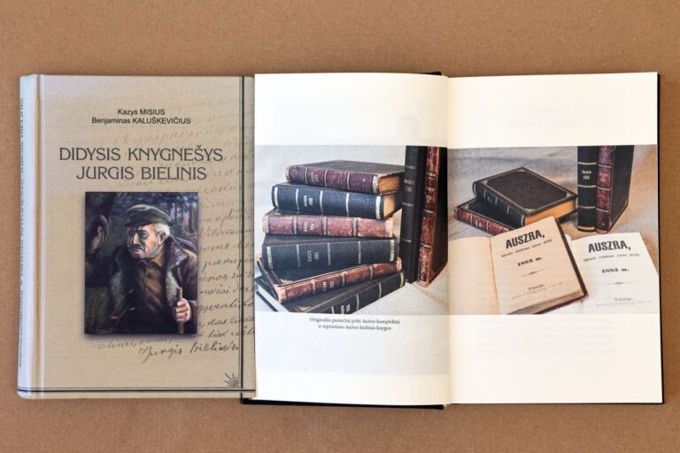 Guli knyga apie knygnešį Jurgį Bielinį, šalia atversta knyga su knygų iliustracijomis