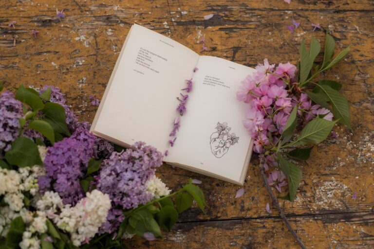 Ant pagrindo su nutrupėjusiais dažais guli atversta knyga apdėliota žydinčiomis gėlėmis