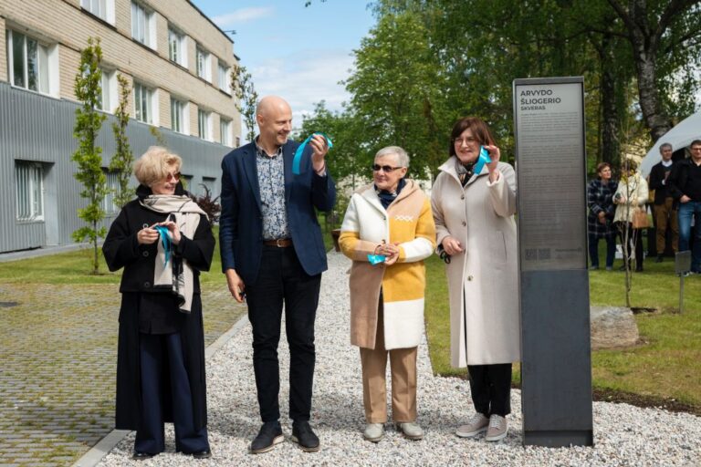 Keturi žmonės stovi ir laiko sukarpytą juostelę po gabaliuką parko fone