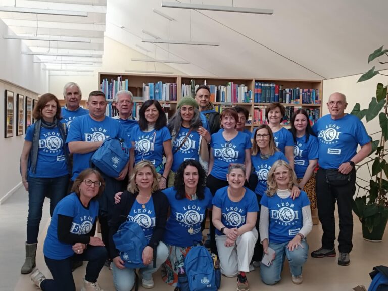 Grupė žmonių vienodais mėlynais marškinėliais tupi ir stovi bibliotekos aplinkoje