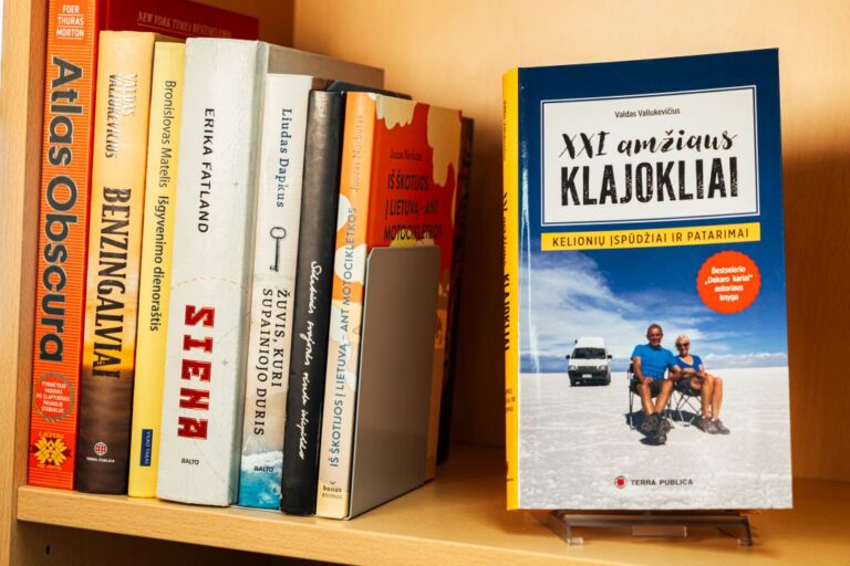 Lentynoje išdėliotos knygos nusuktais viršeliais, viena jų atsukta viršeliu į žiūrovą