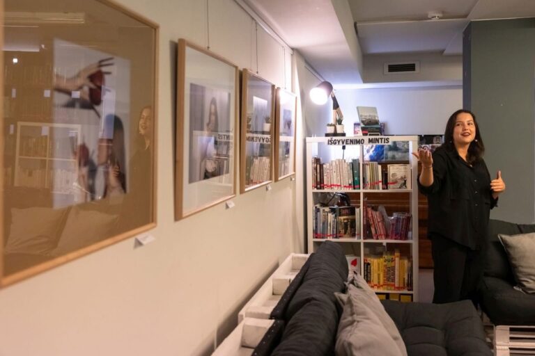 Mergina rodo ranka į ant sienos kabančią įrėmintą nuotraukų kompoziciją