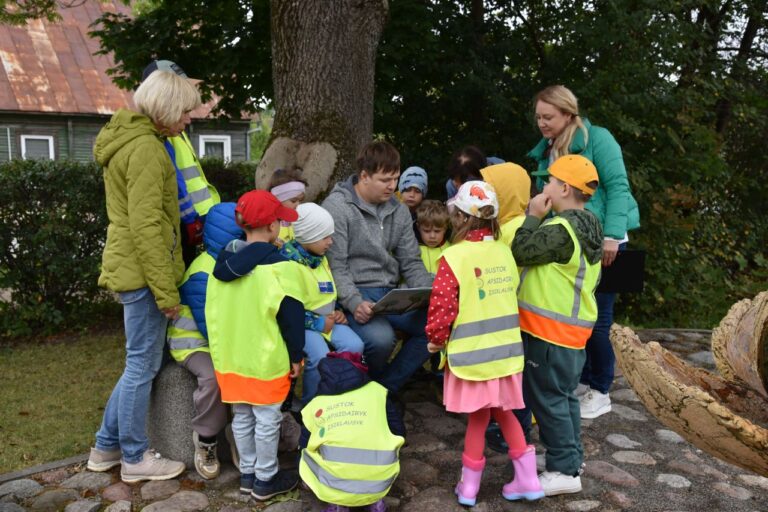 Tėčiai skaitė vaikams Vyras skaito knygą ratu apstotas vaikų lauko aplinkoje
