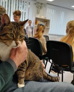 Katinas tupi vyrui ant kelių sėdinčių vaikų fone