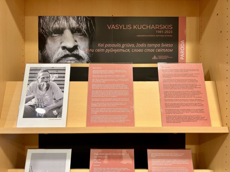 Lentynose išdėliotos nuotraukos ir parodos pristatymo lapai