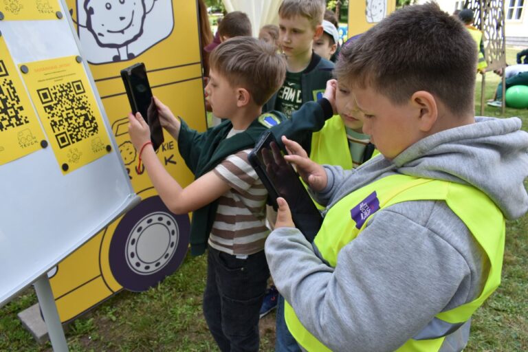 Vaikai su mobiliaisiais telefonais skenuoja QR kodą ryškaus geltono furgonėlio fone