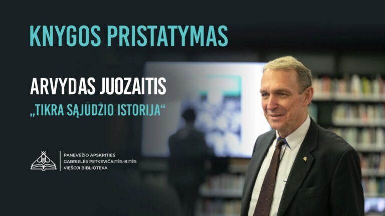 Filosofas Arvydas Juozaitis su kostiumu stovi ekrano fone salės erdvėje