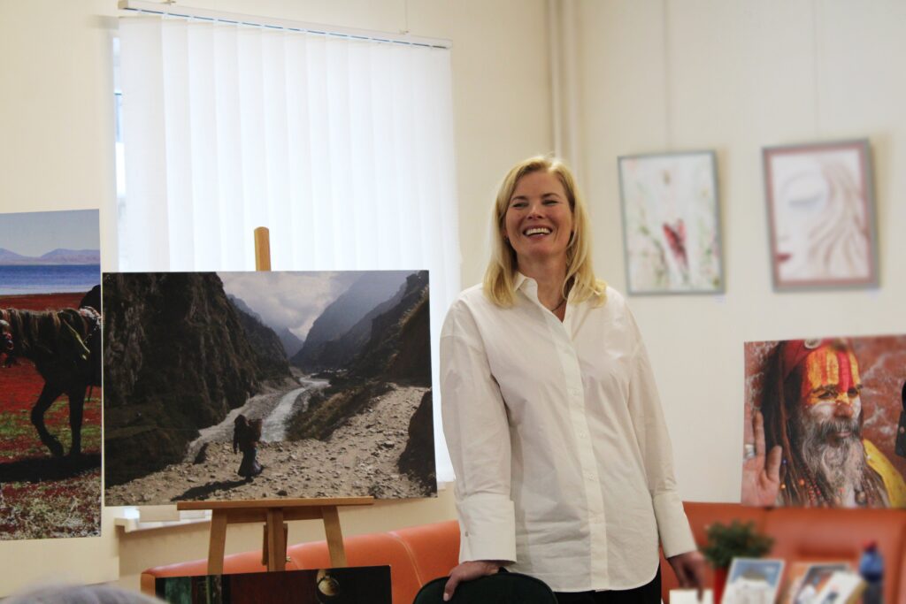 Nuotraukoje matoma moteris, šypsodamasi stovinti prie nuotraukos su kalnų slėniu ir upe. Ji vilki baltus marškinius ir atrodo laiminga bei atsipalaidavusi. Už jos matomos įvairios meno kūriniai ir nuotraukos, įskaitant žmogų su raudonais dažais veide.
