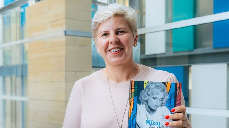 Besišypsanti moteris trumpais plaukais su knyga rankose bibliotekos fone