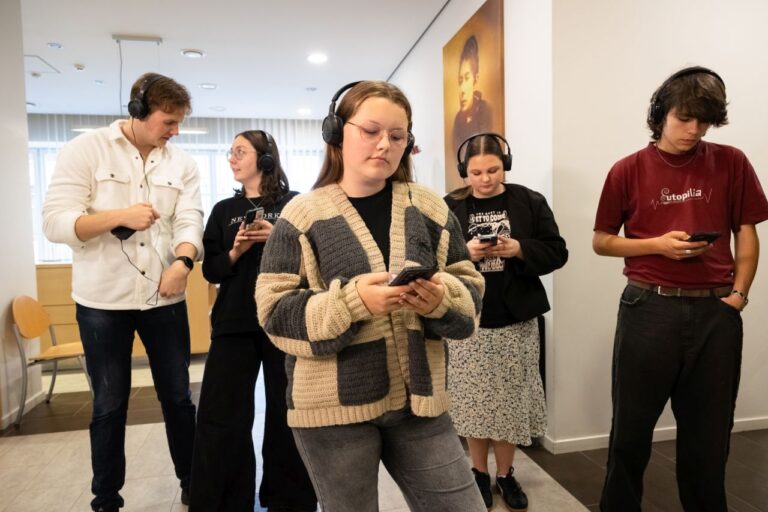 Jaunimas telefonuose klausosi audiogido įrašų bibliotekos erdvės fone