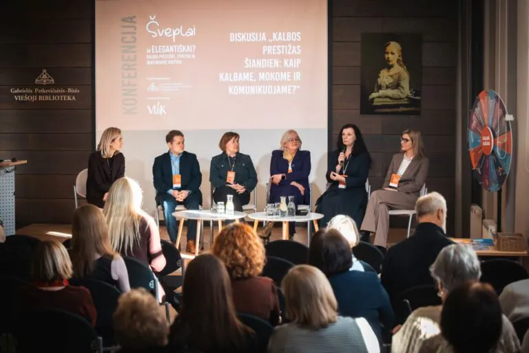 Šeši konferencijos lektoriai sėdi puslankiu priešais renginio auditoriją ir diskutuoja bibliotekos salės fone